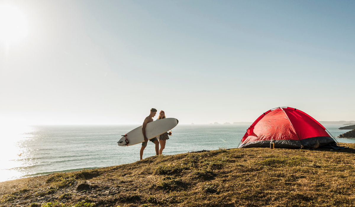 Young-couple-with-surfboard-camping-at-seaside-ee220324