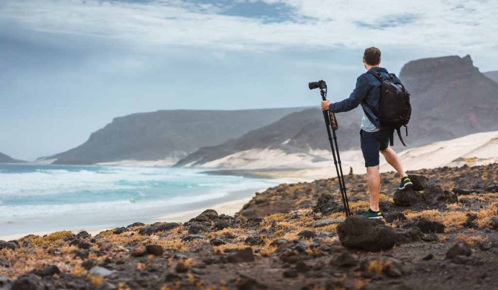 photographer in the beach holding his tripod with camera - ee220330