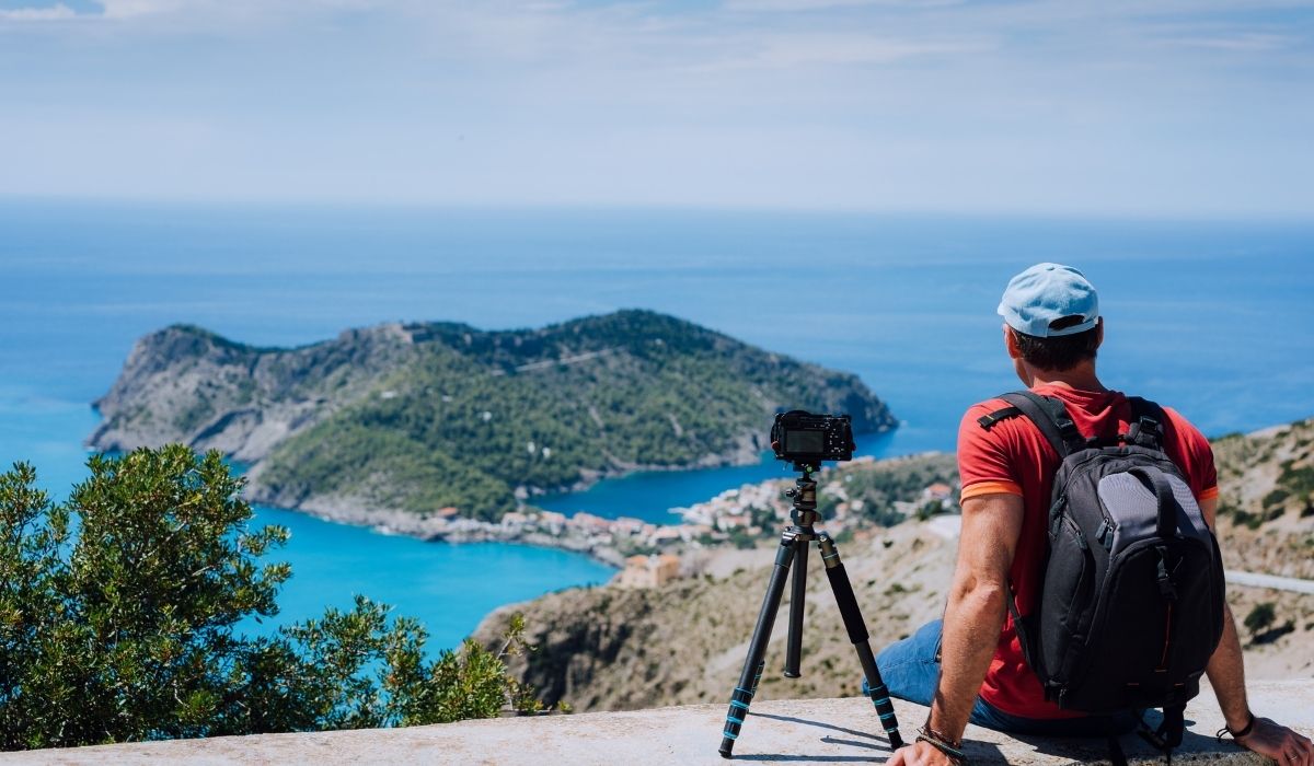 photographer wearing a backpack and his camera on tripod beside him while enjoying the view - ee220330