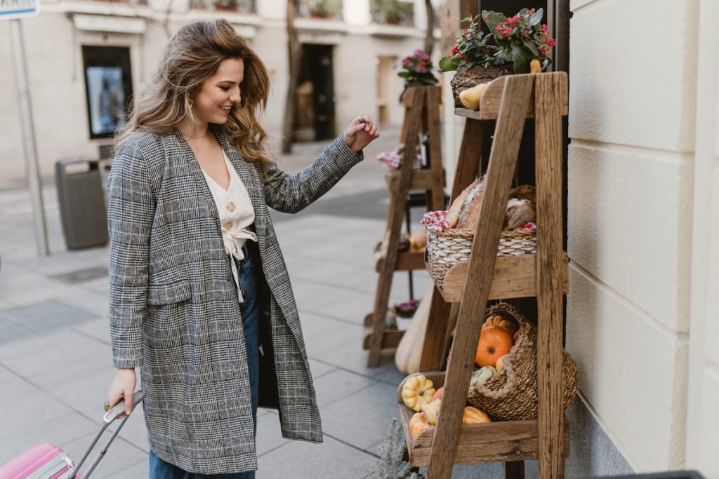 Smiling female tourist near grocery shop with her pink suitcase