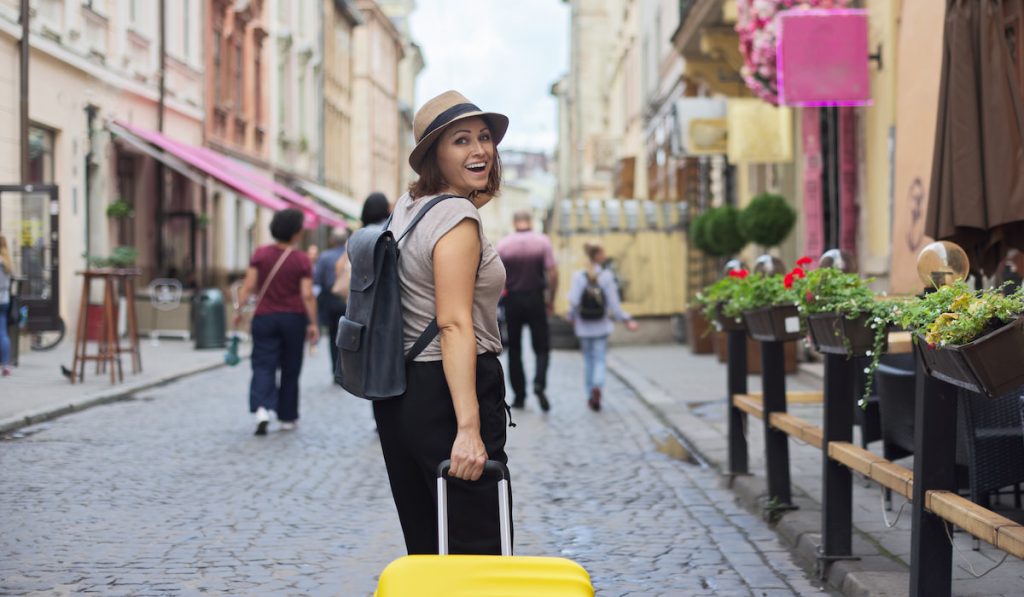 adult smiling woman travelling in tourist city with suitcase 
