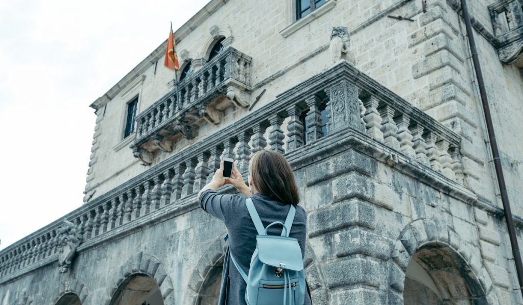 back of young woman with blue backpack taking picture of museum