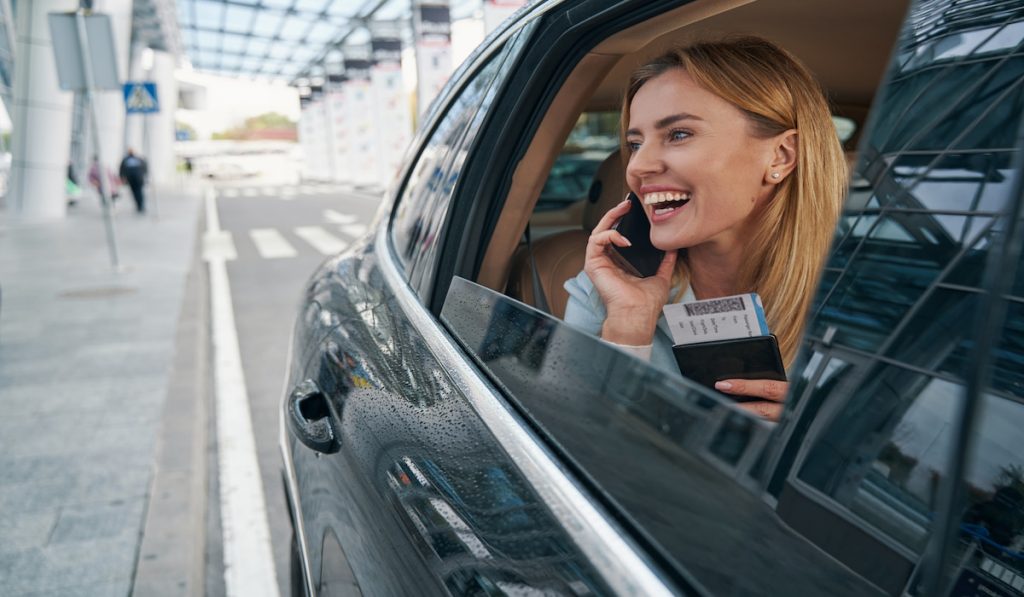 cheerful traveler in the car holding her passport while talking to her mom on the phone