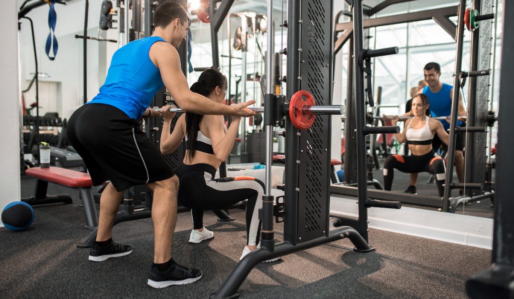 gym instructor helping woman lifting 