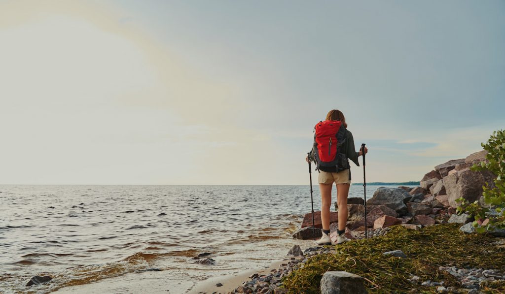 woman backpacker by the beach hiking holding hiking sticks