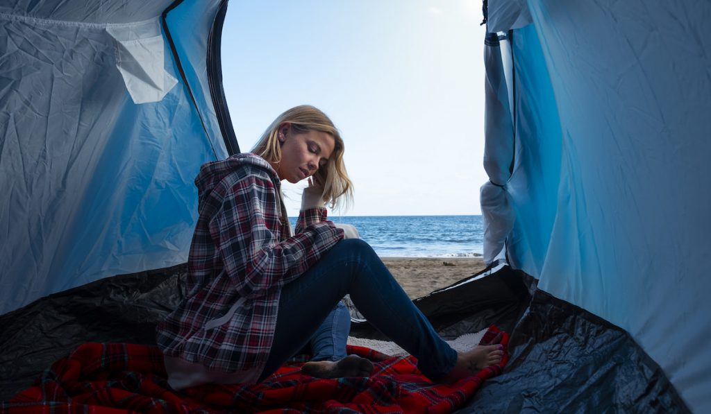 young hipster lady traveling alone in free camping tent at the beach
