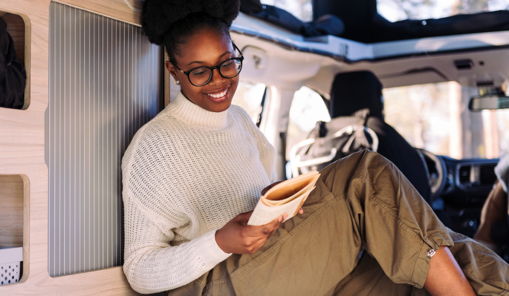 smiling woman relaxing in camper van reading book
